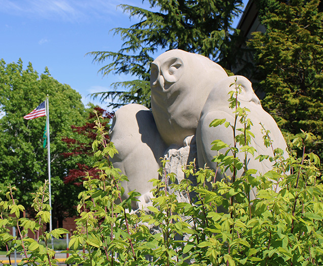 Three owl statue with USA flag in background summer foliage around