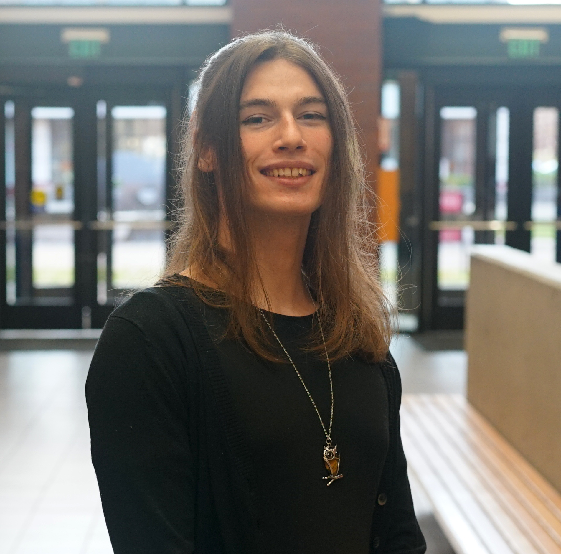 Stella standing in the Heiner foyer. She is smiling with brown medium length hair and is wearing a black long-sleeve top