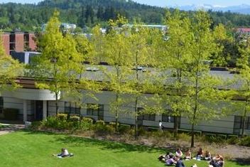 Baker Hall with students sitting on grass in front of building, and trees with green leaves along front pathway